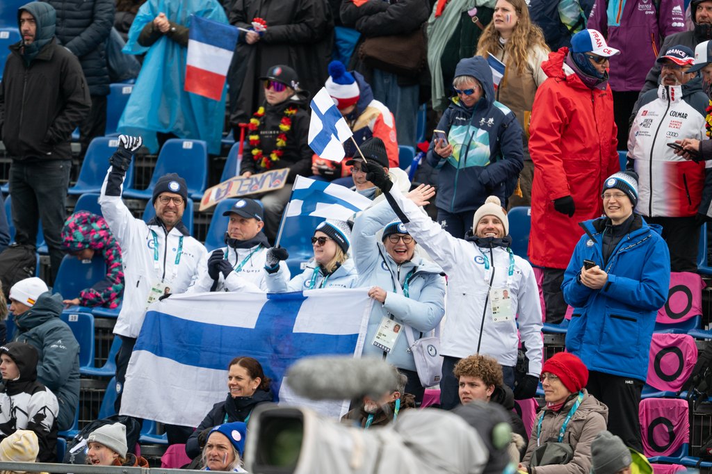 Iloinen suomalaisyleisö Suomen lippujen kanssa kannustamassa.
